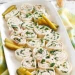 Homemade ham and cheese tortilla pinwheels and pickle spears on a platter.