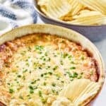 Cheesy baked hot onion dip with a potato chip dipping into it.