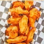 A parchment paper-lined basket filled with Louisiana hot sauce wings.