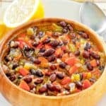 A bowl of copycat Panera black bean soup, lemon halves, and a spoon on a plate.