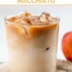 A glass of copycat Starbucks apple crisp macchiato, cinnamon sticks, and an apple.