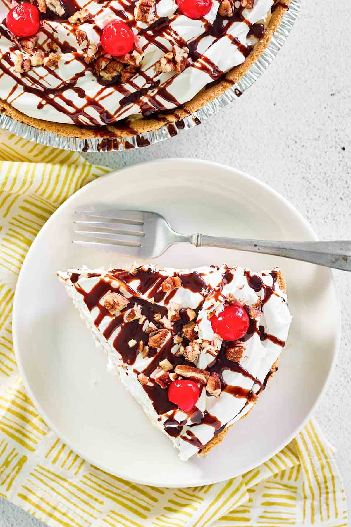 Pineapple banana pie topped with whipped cream, pecans, cherries, and fudge sauce.