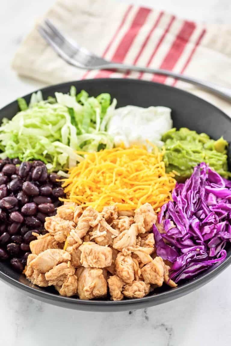 Bowl with Mexican seasoned chicken, black beans, cheese, rice, and fresh toppings.