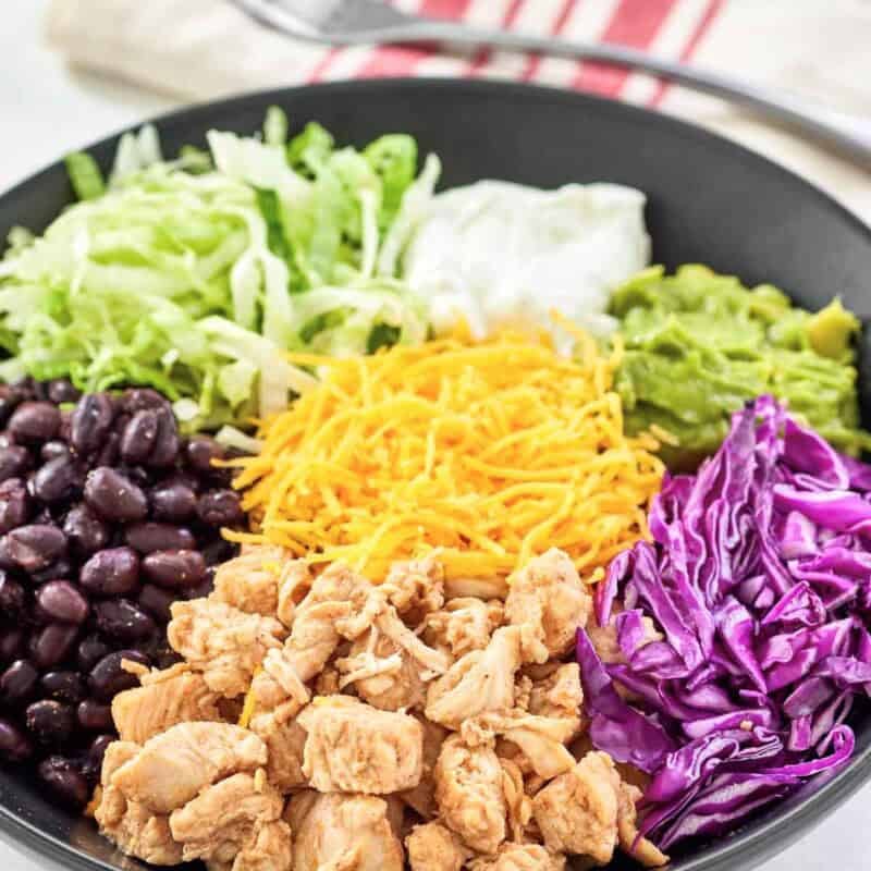 Bowl with Mexican seasoned chicken, black beans, cheese, rice, and fresh toppings.