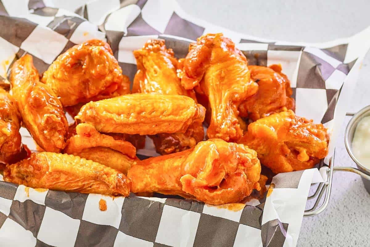 Hot sauce tossed chicken wings served in a parchment paper-lined basket.