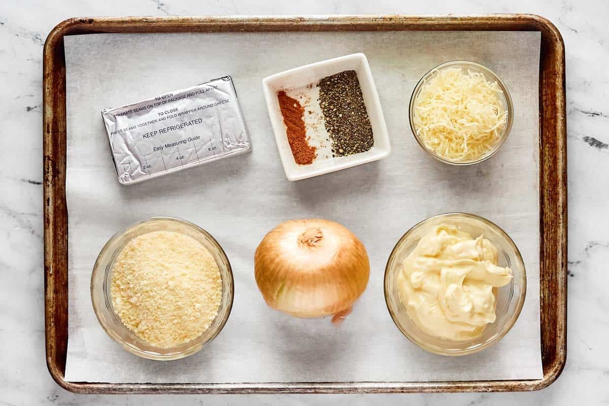 Onion, cheeses, mayonnaise, and seasonings on a tray.