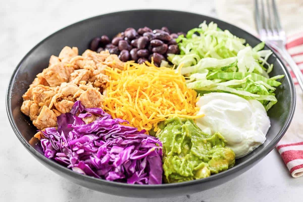 Seasoned chicken, black beans, cheese, and- more toppings over rice in a bowl.
