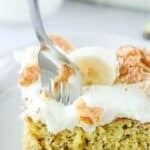 A fork in a slice of banana cake with cream cheese frosting.
