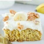 A slice of banana cake with cream cheese frosting garnished with a banana and nuts.