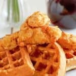 Copycat Grand Lux Cafe chicken and waffles on a plate and a pitcher of syrup behind it.