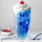 Copycat Ruby Tuesday Smurf Punch with whipped cream and a cherry on top in a tall glass.