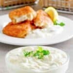 A small bowl of homemade tartar sauce and the sauce served with fish sticks on a plate.
