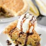 A slice of classic Toll House Pie with a scoop of vanilla ice cream and chocolate drizzle on top.