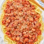 Spaghetti noodles topped with hot dog tomato sauce on a platter.
