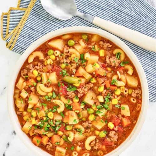 Tomato, ground beef, potato vegetable, and pasta soup in a large bowl.