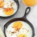 Oven-baked eggs in small cast iron skillets and a glass of orange juice.