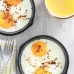 Two small cast iron skillets with oven baked eggs in them.