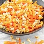Homemade Cheetos popcorn in a serving bowl and scattered in front of it.