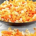 Homemade Cheetos popcorn in a bowl and scattered in front of it.