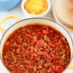 Homemade Indiana-style chili in a Dutch oven and a bowl of shredded cheese behind it.