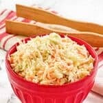 Copycat KFC coleslaw in a small bowl and wooden salad tongs on a napkin behind it.