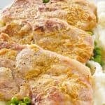 Three mustard crusted baked pork chops on top of peas and mashed potatoes.