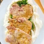 Mustard crusted baked pork chops over peas and mashed potatoes on a platter.